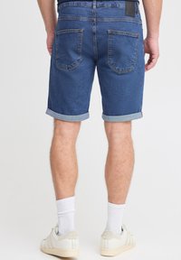 Džinsu šorti vidēji zilā tonī ar uzlocītām malām, divām aizmugurējām kabatām un ādas plāksnīti pie jostasvietas.