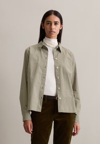Groen en wit geruite overhemden met een kraag, gecombineerd met een witte top met hoge hals en gestructureerde bruine corduroy broek.