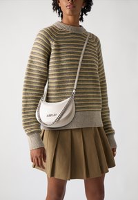 Sac en cuir gris clair porté en travers avec une chaîne en argent, présentant le mot "REPLAY" en relief. Associé à un pull en tricot rayé et une jupe plissée.
