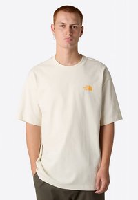 Bawełniany t-shirt w kolorze kremowym o luźnym kroju, krótkich rękawach i małym pomarańczowym logo na górnej lewej stronie klatki piersiowej.