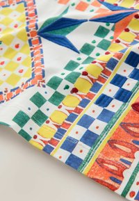 Colorful fabric with geometric patterns including blue and green diamonds, yellow circles, red dots, and orange shapes, stitched at the edge.