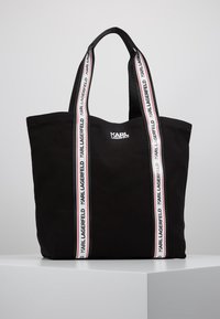 Svart tote-väska med två vita axelremmar som har texten "KARL LAGERFELD" i svart, samt "KARL LAGERFELD"-logotypen i vitt på framsidan i mitten.