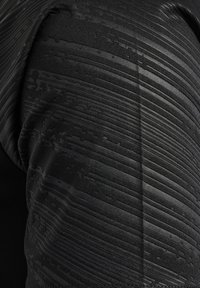 Primer plano de tela negra con líneas horizontales y diagonales texturizadas que crean un patrón geométrico sobre una superficie curva.