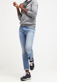Grå fleece hoodie med cowl-neck, ljusblå denimjeans och svarta sneakers med vita snörningar. Avslappnad sportig stil.