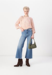 Világos rózsaszín, texturált mintázatú kötött felső, széles szárú kék farmernadrággal párosítva. Barna sarkú bokacsizma és zöld táska teszi teljessé a megjelenést.