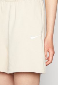 Beiga Nike-shorts gjorda av mjukt bomull med elastisk midja. Har en liten vit Nike swoosh-logotyp på vänster sida.