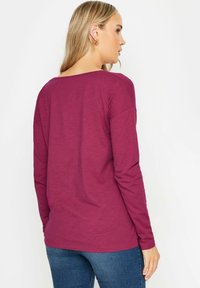 T-shirt z długim rękawem w kolorze burgundowym, wykonany z miękkiego materiału, o Luźnym kroju, z szerokim dekoltem i lekko opuszczonymi ramionami.