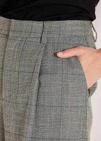 Hand auf der Seitentasche einer grauen karierten Hose, mit einem schwarzen Oberteil, das eingesteckt ist.