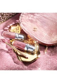 Deux gloss à lèvres roses Kiko Milano, un crayon à lèvres et une trousse de maquillage pailletée rose sur une surface rose scintillante avec un plateau doré.