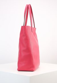 Sac fourre-tout en cuir rose avec une surface texturée, de forme rectangulaire haute, et deux poignées. Aucune quincaillerie ou accent visible.