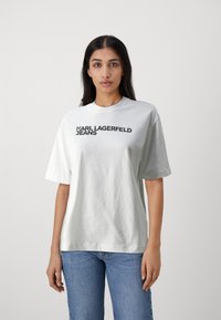 Camiseta de algodón blanca con mangas cortas, escote redondo y texto impreso en negro que dice "KARL LAGERFELD JEANS" en el pecho.