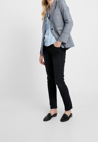 Šedý kostkovaný blazer přes světle modrou blůzu, doplněný o černé přiléhavé kalhoty a černé nazouvací boty. Blazer má dvoucestné zapínání.