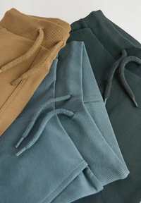 Tre par joggingsbyxor i khaki, blå och mörkgrön. Tillverkade av bomull med ribbade midjeband och platta snören. Slät textur.