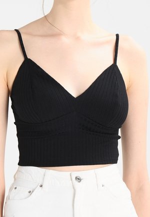 Woman wearing a ribbed black cropped camisole top with thin straps and white high-waist jeans, shown from shoulders to waist.