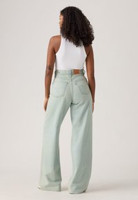Light green high-waisted wide-leg jeans made of denim, featuring a back patch and metal button closure, displayed from the rear.