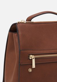 Bruine leren handtas met een gestructureerde afwerking, voorzien van een bovenhandvat, gouden rits en een externe ritszak. 