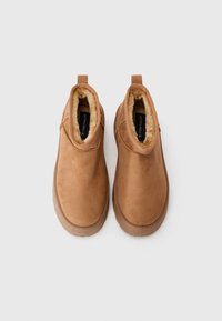 Bottines en daim marron avec une doublure en fourrure douce, des côtés élastiques et une semelle en caoutchouc texturée pour une bonne adhérence. Présente une languette à l'arrière.