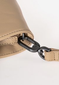 Sezione di una borsa in pelle marrone chiaro con una clip metallica nera. La cucitura è visibile e c'è una superficie liscia sulla pelle.