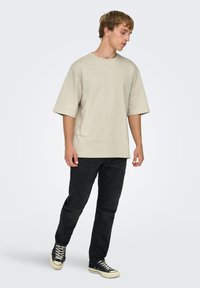 T-shirt beige oversize à manches courtes, associé à un jean noir et des baskets montantes noires. Tissu doux et coupe décontractée.
