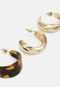 Trois paires de boucles d'oreilles créoles : une en or brillant, une en or texturé et une en écaille de tortue avec une finition lisse. Toutes disposent de tiges en métal.