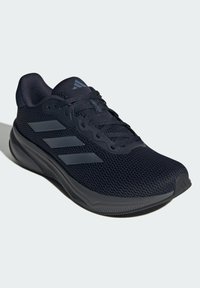 Zapatilla deportiva negra con parte superior de malla, tres rayas grises en el costado, suela texturizada y cuello acolchado para mayor comodidad y soporte.
