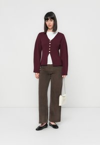 Bordeaux gebreide cardigan met lange mouwen en een V-hals, voorzien van vijf knopen aan de voorkant. Draag het over een wit topje en gecombineerd met een bruine broek.