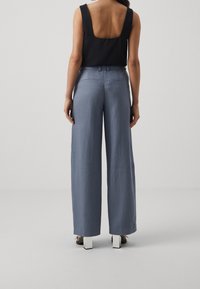 Pantaloni a gamba larga in tessuto azzurro chiaro, con una superficie liscia, tasche posteriori e una vestibilità sartoriale. Abbinati a un top senza maniche nero.
