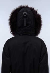Sort parka jakke med en aftagelig hætte, der har en tyk, mørk faux fur pynt, justerbar rygstrop og en glat tekstur.