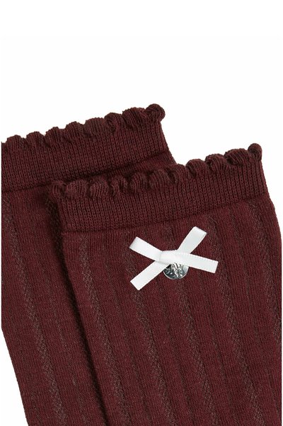Chaussettes bordeaux côtelées avec des poignets froncés, décorées d'un petit nœud blanc et d'un charm argenté rond.