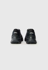 Black athletic shoes with a textured fabric upper, padded collar, and cushioned sole. Features reflective detailing on the heel and tongue.