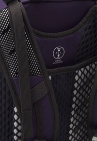 Purple and black backpack featuring mesh accents, adjustable straps, and a tag indicating height adjustment functionality.