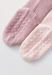 Rosa Baumwollsocken mit strukturiertem Rippenmuster, die an den Sohlen mit Silikonpunkten für besseren Halt ausgestattet sind. Eine Socke ist leicht dunkler als die andere.