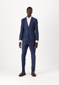 Dark blue suit with a slim fit, textured fabric, single-breasted jacket, two buttons, and contrasting white shirt. Brown dress shoes.