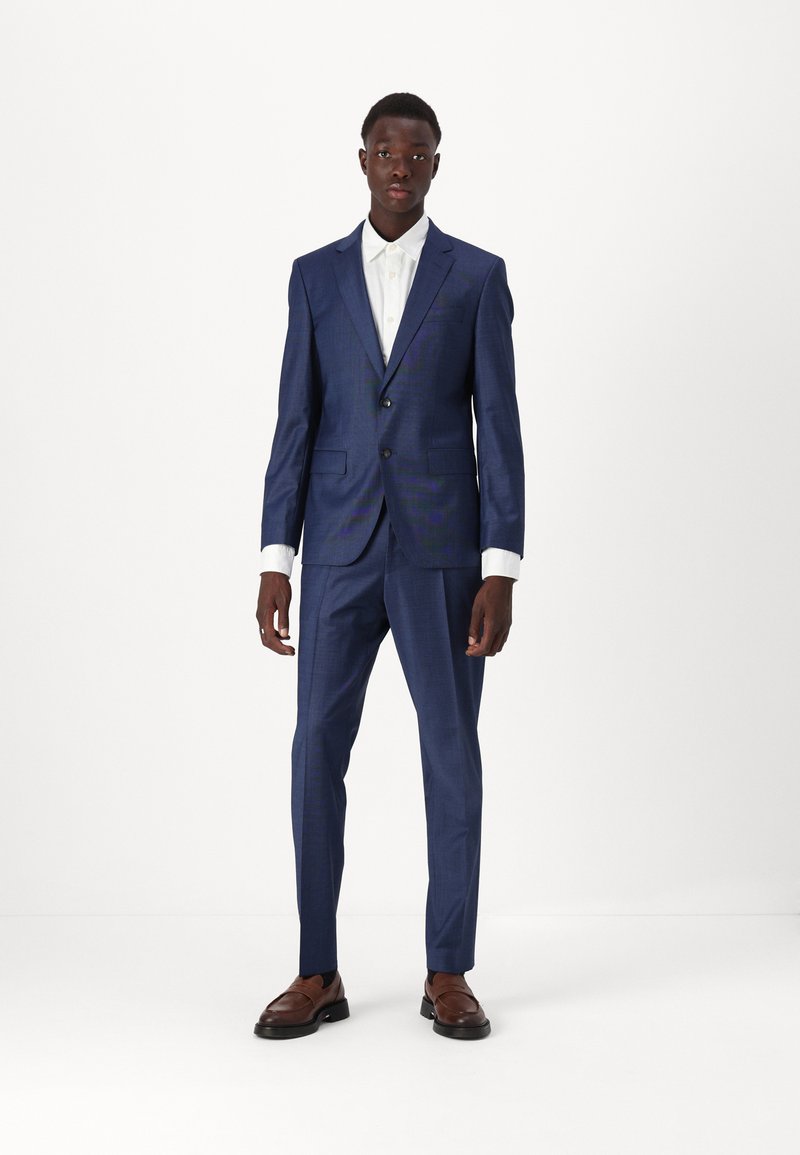 Dark blue suit with a slim fit, textured fabric, single-breasted jacket, two buttons, and contrasting white shirt. Brown dress shoes.