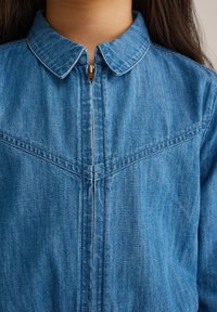 Modra jeans jakna z ovratnikom, sprednjim zadrgo in izrazitimi šivi. Mehka tekstura z sproščenim dizajnom.