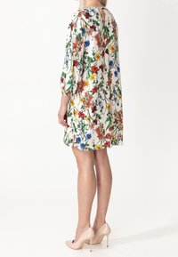 Blommig klänning i ett lätt tyg, med färgglada blommor i röd, blå, gul och grön mot en krämfärgad bakgrund. ¾ ärmar och lös passform.