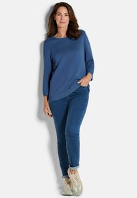 Blauer strukturierter Pullover mit rundem Ausschnitt, kombiniert mit schlanken blauen Jeans und hellen Sneakern mit beigem Muster.