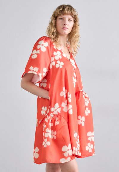 Robe corail en tissu lisse, avec un décolleté en V, des manches courtes, un motif floral, deux poches latérales et un ourlet froncé.