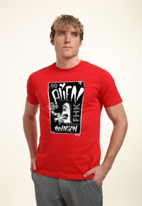 Rød bomulds t-shirt med en sort-hvid grafisk design med teksten "ALIEN INVASION" og en abstrakt alien-illustration.