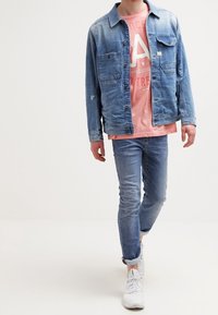 Jasnoniebieska kurtka dżinsowa z kieszeniami na piersi; różowy t-shirt z grafiką; jasnoniebieskie dżinsy; białe trampki. Swobodny strój w warstwowym stylu.