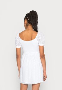 Vit klänning med puffärmar, broderat mönster, åtsittande midja och utsvängd kjol. Har en fyrkantig rygg med urringning och strukturerad tyg.