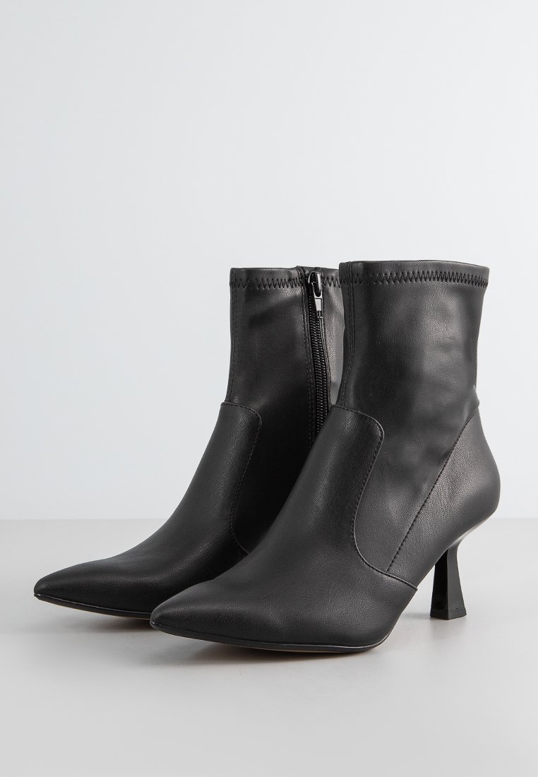 Ein Paar schwarze Lederstiefeletten mit spitzer Zehenpartie, mittelhohen, schrägen Absätzen und seitlichen Reißverschlüssen auf einer schlichten Oberfläche.