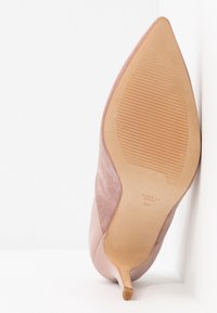Talons aiguilles en daim rose avec un bout pointu et un talon fin. Semelle texturée avec les informations de la marque imprimées, doublure en cuir lisse.