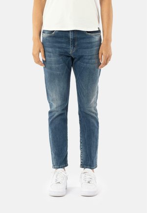 Blauwe denim jeans met een rechte pasvorm, lichte vervaging, vijf-pocket ontwerp. Gecombineerd met witte sneakers, gepresenteerd tegen een effen achtergrond.