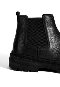 Bottine Chelsea en cuir noir avec panneau texturé, côtés élastiques, et semelle en caoutchouc avec un motif strié pour une meilleure adhérence.