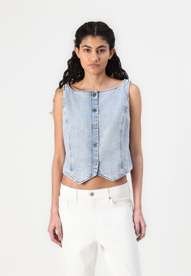 Himmelblaues Denim-Crop-Top mit Rundhalsausschnitt, sieben vertikalen Knöpfen und spitzem Saum. Wird über weißen hoch taillierten Hosen getragen.