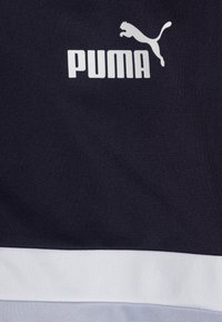 Abbigliamento sportivo Puma in tessuto blu navy scuro con superficie testurizzata, con logo bianco e strisce di accento azzurro chiaro contrastanti nella parte inferiore.