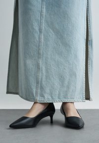 Black leather pumps with a pointed toe and a moderate heel, paired with a light blue denim skirt featuring side slits and visible stitching.