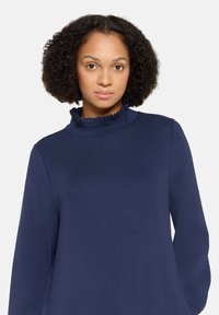 Marineblaues Langarm-Top mit hohem, gerafftem Kragen. Glatte Baumwollstruktur, mit lockerem Schnitt und einfachem Design.