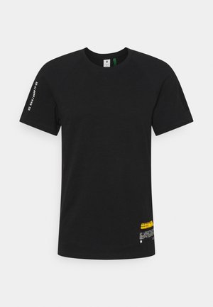 Schwarzes kurzärmliges T-Shirt mit Rundhalsausschnitt, mit weißem Text auf dem linken Ärmel und weißem sowie gelbem Text in der Nähe des unteren rechten Saums.